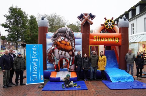 Gruppenfoto vor der neuen Wikingerhüpfburg am Capitolplatz: Stefan Wesemann (IHK), Helge Schütze (Stadtmarketing), Hanns-Peter Arp (Zukunftsbeirat Schleswig Fonds), Björn und Marta Danczak (M. B. D. Hüpfburgenvermietung), Torge Nehls (Helios Klinik), Josephin Schäfer (Stadt Schleswig), Thomas Forck (Schuhgeschäft Forck, IGL) und Rowena Sandmeier (Stadt Schleswig).