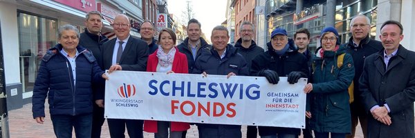Mitglieder des Schleswig Fonds halten stehen in der Innenstadt mit einem Plakat "Schleswig Fonds"