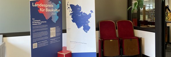 Im Eingangsbereich der Stadtbücherei weisen große Pappaufsteller auf die Ausstellung Landespreis für Baukultur 25.–30.03.2026 hin