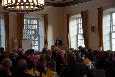 Ehemalige Mitarbeitende beim Ehemaligen-Kaffee am 19.11.2024 im historischen Ständesaal. Der stellvertretende Bürgermeister Rainer Haulsen spricht ins Mikrofon.