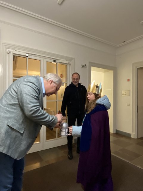 Stephan Dose steckt einen Geldschein in das Sparschwein von Matilda Zydek. Im Hintergrund schaut Pastor Winter zu.