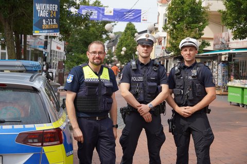 Ein Mitarbeiter des Kommunalen Ordnungsdienstes mit zwei Polizisten neben einem Polizeiauto im Stadtweg in Schleswig.