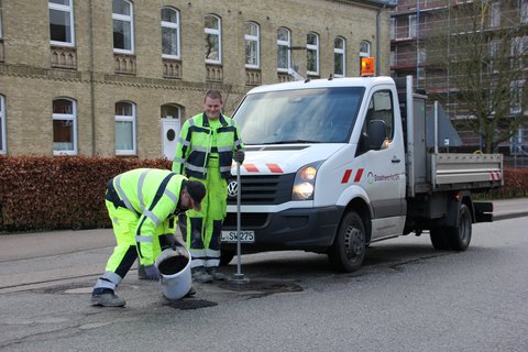 Bild zeigt Mitarbeitende der Stadtwerke SH bei der Reparatur eines Schlagloches in der Moltkestraße mit Kaltasphalt