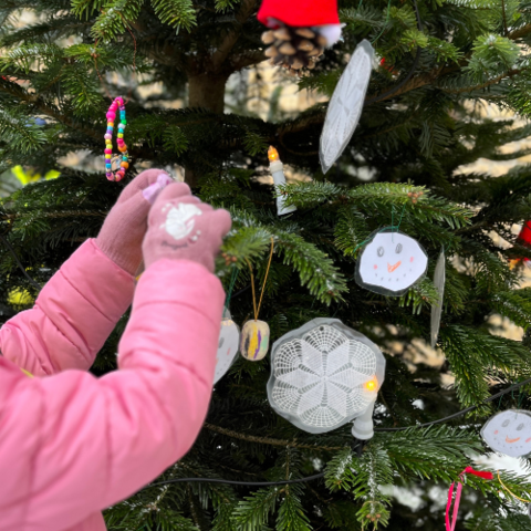 Foto zeigt Kinderhände, die den Weihnachtsbaum schmücken