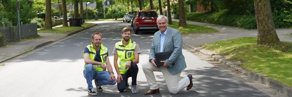 Torben Krüger, Fabian Hundertmark und Bürgermeister Stephan Dose knien auf der sanierten Kastanienallee