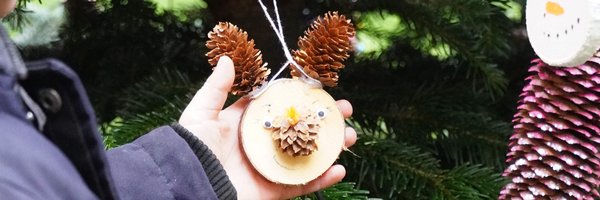 Ein Kind beim Weihnachtsbaumschmücken mit einem gebastelten Rentier-Weihnachtsbaumanhänger.